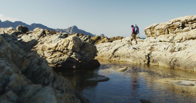 Biracial man with prosthetic leg trekking on rocks by the sea wearing backpack. Long distance walking, fitness, challenge, disability, nature and healthy outdoor lifestyle.