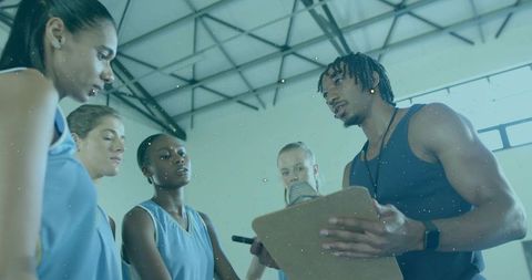 Basketball coach leading timeout huddle with players holding clipboard in gym