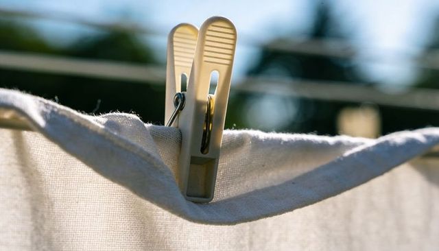 Sunlit plastic clothespin gripping white sheet on clothesline with soft bokeh