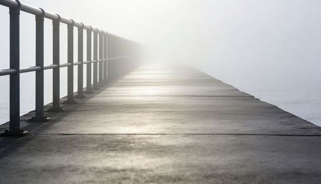 Concrete pier leading into dense fog with metal railing minimalist seascape perspective