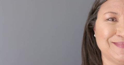 Smiling mature woman half-face portrait on neutral gray background with copy space studio headshot