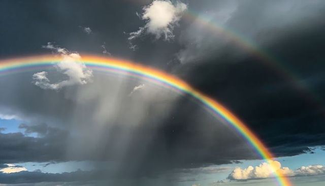 Vivid Double Rainbow Arching Over Storm Clouds with Sunbeams and Rainfall