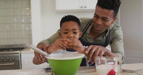 Father teaching son cracking egg while baking together in bright home kitchen