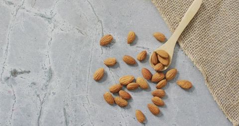 Raw almonds on light grey countertop with wooden spoon