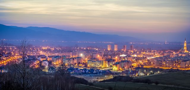 Panoramic evening view of a modern city with glowing lights illuminating the skyline against the soft twilight sky. Perfect for use in travel promotions, urban lifestyle blogs, real estate advertisements, and architectural showcases.
