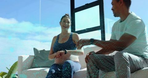 Couple happy wearing smartwatches checking fitness trackers on couch in living room
