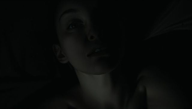 Moody low-light portrait woman lying on bed, chiaroscuro shadows, intimate closeup