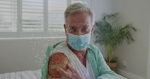 Senior man wearing surgical mask receiving vaccination and showing bandage on upper arm
