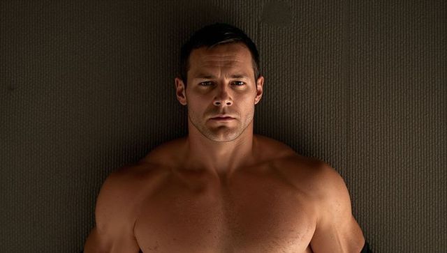 Lying shirtless muscular man displaying chiseled torso overhead on ribbed exercise mat