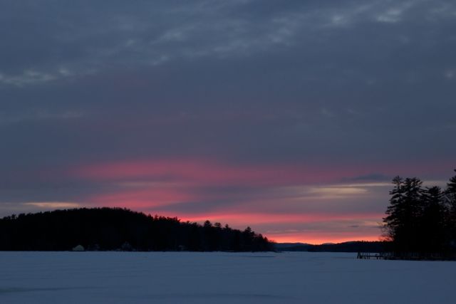 Beautiful winter sunset over frozen lake with snowy landscape, and pink hues in the sky. Ideal for use in travel blogs, nature websites, and calming background settings.
