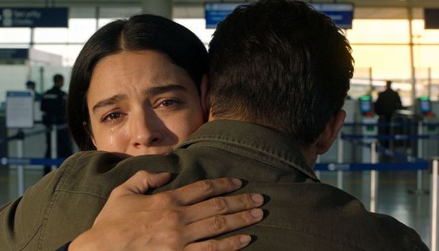 Couple embracing tearful reunion at airport terminal, woman crying in warm sunlight