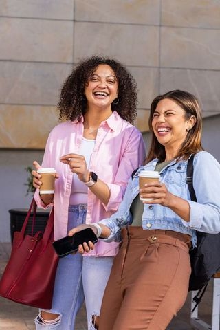 Laughing african american friends holding coffee cups in urban plaza with red tote