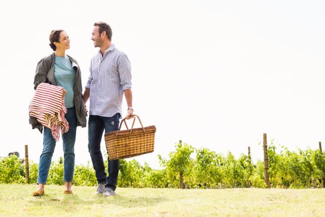 Young couple walking in vineyard carrying picnic basket and blanket. Ideal for promoting outdoor activities, leisure time, romantic getaways, and lifestyle content. Perfect for advertisements, travel brochures, and social media posts highlighting relaxation and nature.