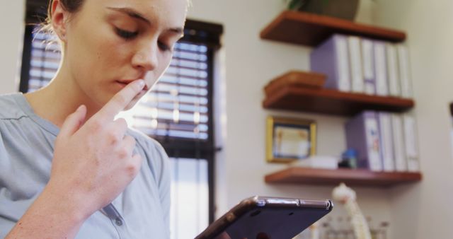 Young woman deep in thought, looking at her smartphone in an office environment. Ideal for themes of technology usage, communication, thinking, problem-solving in modern work settings.