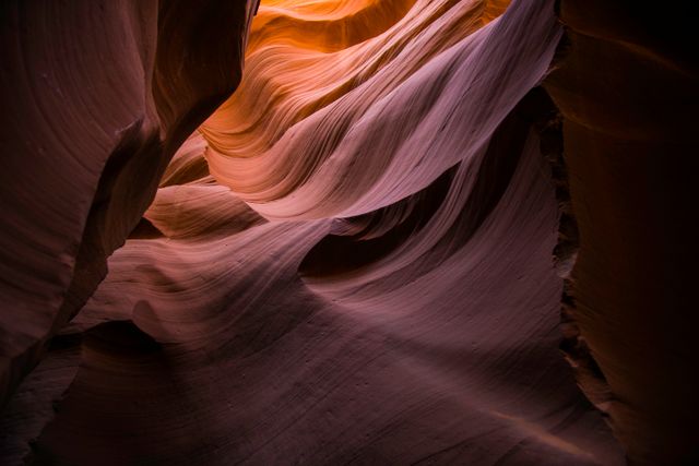 Sunlight illuminates the layered rock formations of a narrow canyon, showcasing its stunning natural beauty. The smooth, undulating surfaces of the sandstone walls present an otherworldly appearance, making this perfect for promoting geology, adventure travel, nature photography, and natural landscapes.