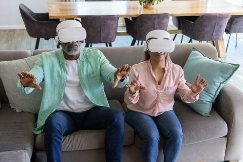 Senior Couple Exploring Virtual Reality Together on Sofa, Hands Reaching into VR World