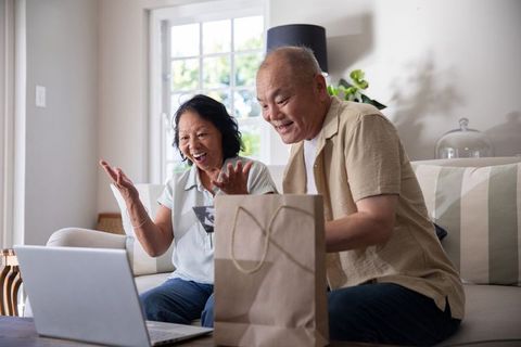 Senior chinese couple video calling and unboxing surprise gift on cozy living room sofa