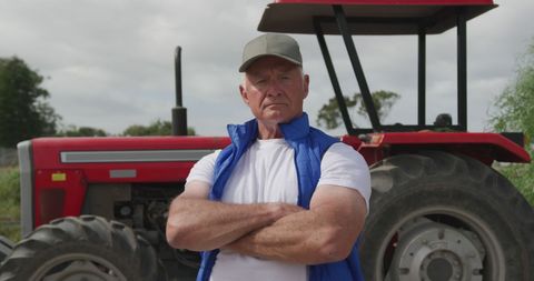 Confident senior farmer standing next to red tractor outdoors