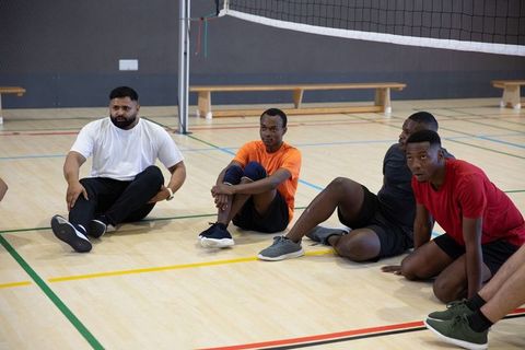 Male volleyball teammates resting on indoor court near net during team training session