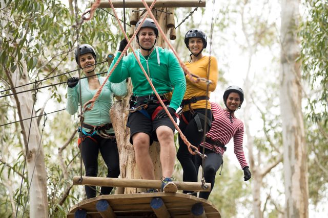 Group of friends standing on a wooden platform in a forest, wearing helmets and harnesses, preparing for a zip line adventure. Ideal for promoting outdoor activities, adventure parks, team-building events, and recreational tourism.