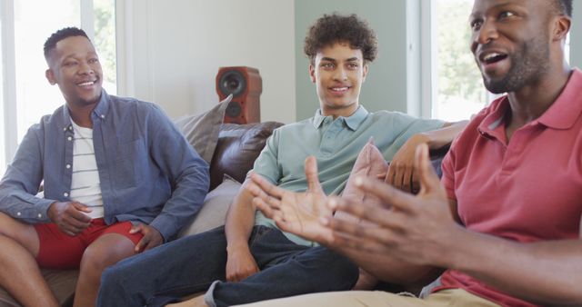 Group of three diverse men sitting and enjoying a casual conversation in a modern living room. They appear relaxed and happy, engaging in a friendly discussion. Ideal for topics related to friendship, bonding, leisure time, social interaction, and modern living spaces. Useful for websites, blogs, and advertisements focusing on community, lifestyle, and home-related content.