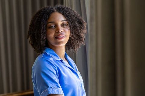African american nurse standing by window in blue scrubs smiling soft natural light