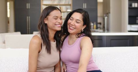 Diverse female relatives leaning and smiling together on cozy sofa in modern kitchen