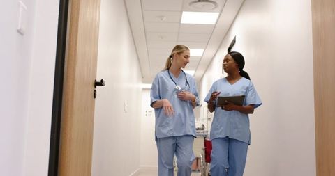 Nurses walking in hospital corridor discussing patient care with tablet and stethoscope