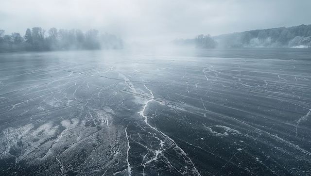 Stretching frozen lake with cracked ice and morning fog conveying winter solitude