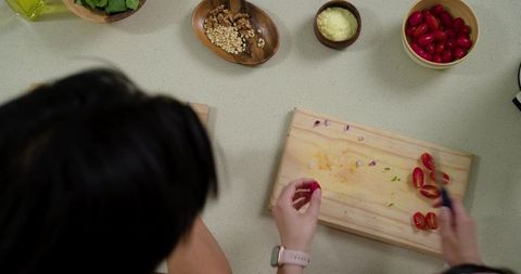 Diverse couple chopping cherry tomatoes on wooden board over speckled countertop