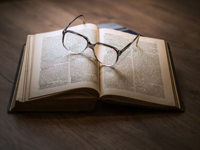 Eyeglasses resting on an open book placed on a wooden floor, illustrating a classic and intellectual scene. Ideal for use in educational materials, literary promotions, blogs on reading habits, and lifestyle articles focusing on learning and relaxation.