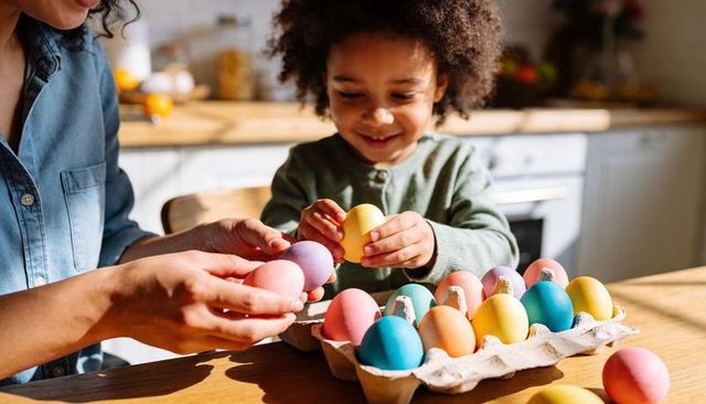 Sunlit spring family decorating pastel easter eggs, child smiling while holding yellow egg