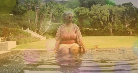 Senior woman sitting poolside, soaking legs in water and relaxing in sunny garden retreat