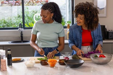 Black women cooking together in modern kitchen chopping fresh vegetables for healthy meal
