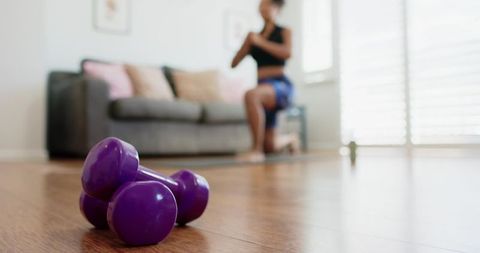 Home workout focus on purple dumbbells with african american woman kneeling