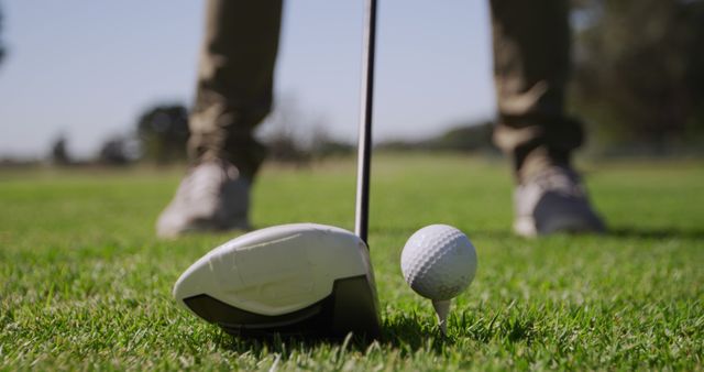 Close-up of a golf ball and club on the course, with copy space. Golfer prepares for a swing on a sunny day at the golf course.