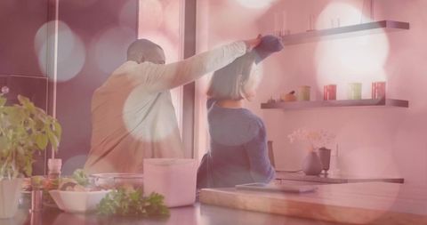 Playful couple measuring head in cozy modern kitchen with bokeh light, fresh herbs and tablet