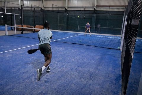 Diverse men playing padel in indoor sports club on blue court lunging and rallying