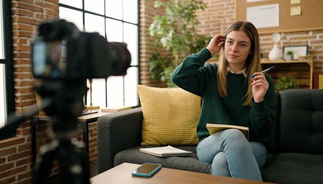 Young woman vlogging from cozy home office with notebook and dslr