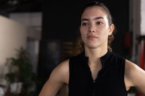Determined female athlete standing in gym wearing black sleeveless zip-top, focused portrait