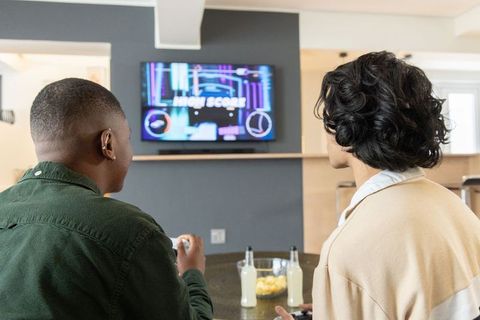 Diverse friends playing video games on tv at kitchen counter sharing snacks and drinks