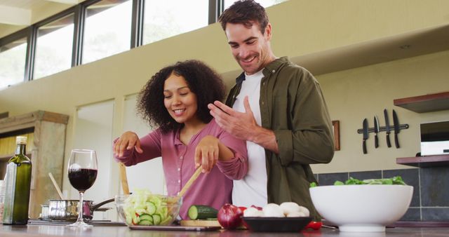 Happy diverse couple preparing a meal together in kitchen, stirring food and laughing. spending free time together at home.
