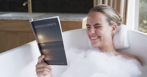 Woman relaxing in bubble bath reading endless sunsets in modern freestanding tub