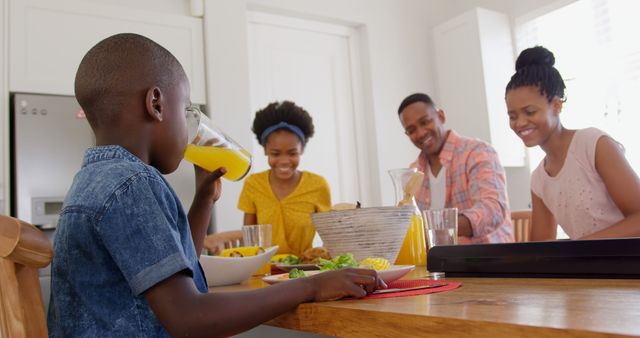 Front view of happy black family eating food on dining table in a comfortable home. Boy drinking juice of glass 4k