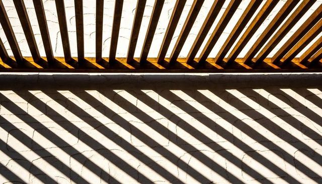 Diagonal Shadow Bands from Wooden Louver Casting on Weathered White Masonry Wall