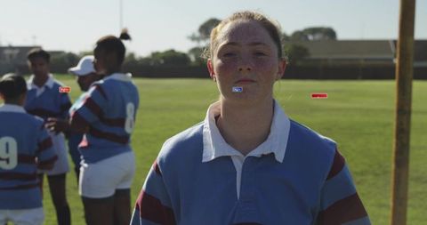 Confident teenage rugby player standing on grass pitch wearing striped blue and maroon jersey