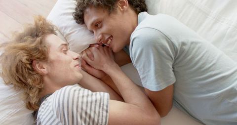 Happy Diverse LGBTQ+ Couple Holding Hands on Bed at Home
