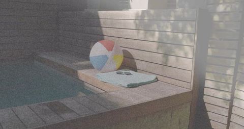 Resting multicolor beach ball on folded mint towel by backyard pool with sunglasses on slatted deck