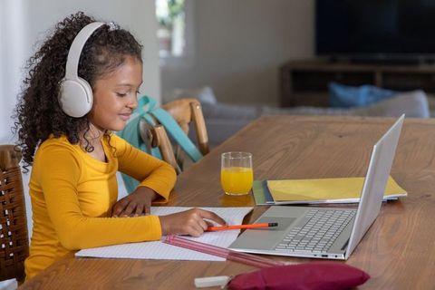 African american girl studying at home with laptop and headphones on sunlit kitchen table