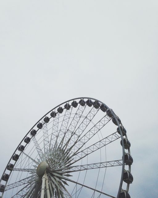 Partially visible Ferris wheel with overcast sky creating a somber and calm atmosphere. Perfect for themes related to amusement parks, outdoor activities, weather conditions, or symbolic representations of circles and rotations. Suitable for travel blogs, brochures, amusement park promotions, and themed graphic design projects.
